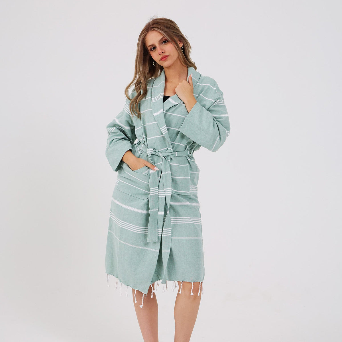 A woman modeling a sage green and white striped cotton bathrobe against a plain white studio background.