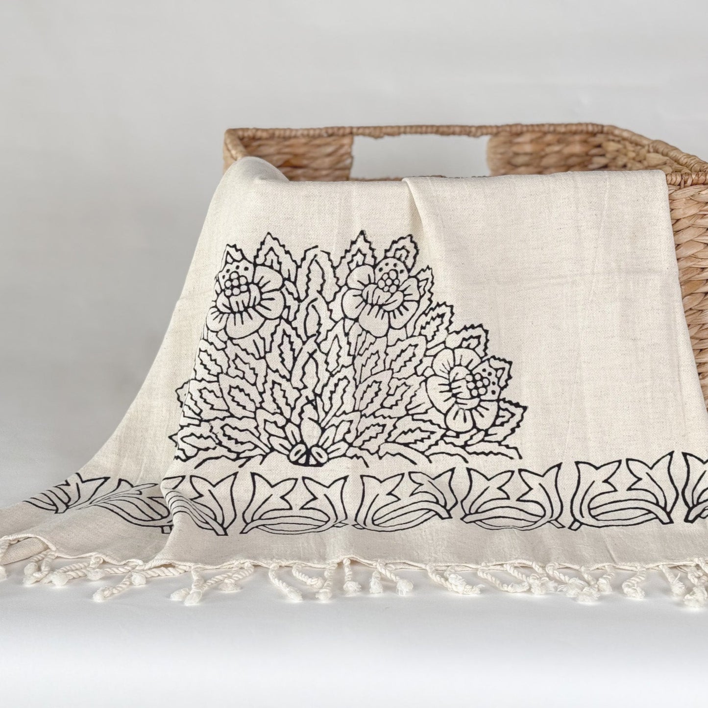 Decorative throw blanket with floral pattern and tassels on a woven basket against a light background