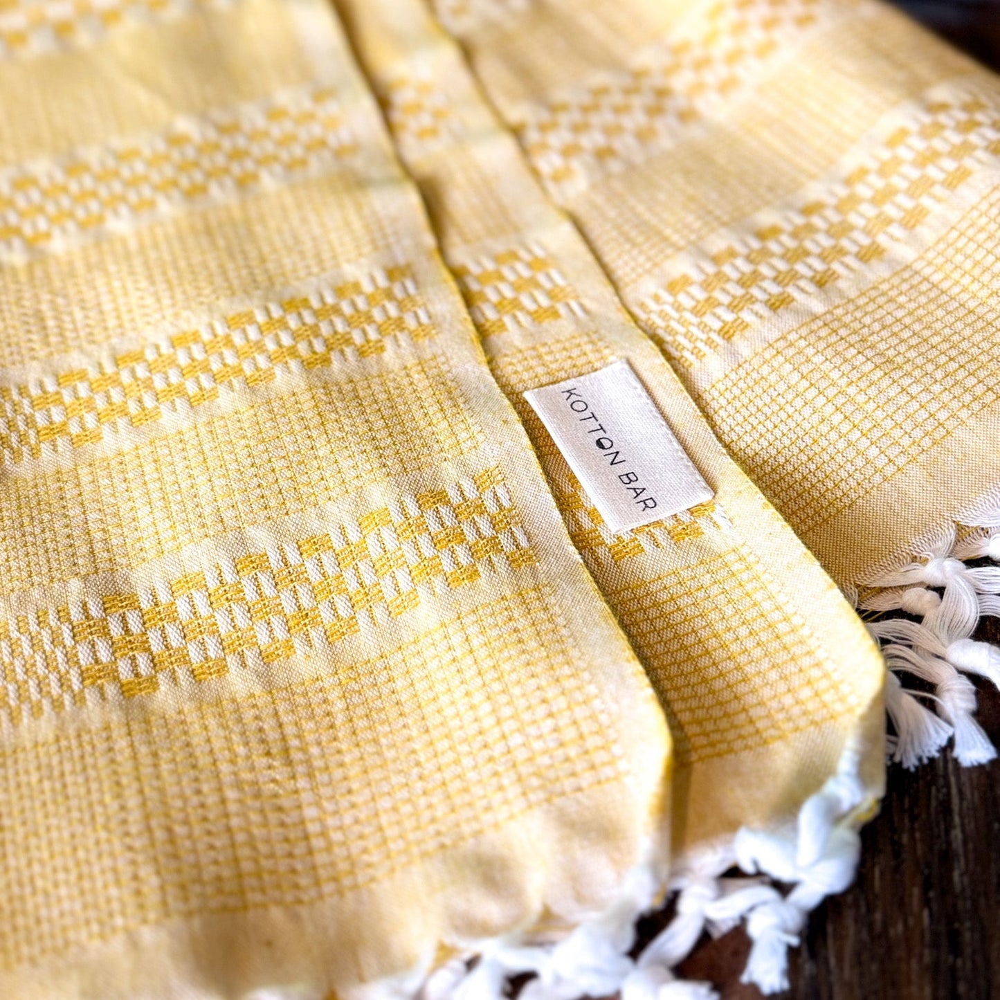 Yellow textured fabric with white lace trim and a brand label on a wooden surface.