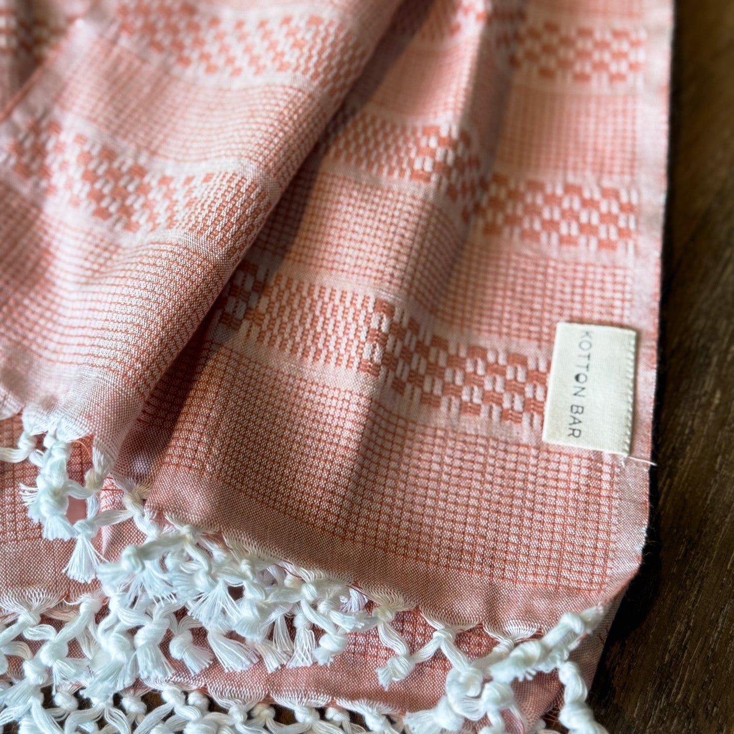 Pink textured fabric with white lace trim and a label on a wooden surface