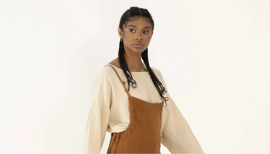 Woman in a cream long-sleeve top and a rust-colored pinafore against a plain light background.