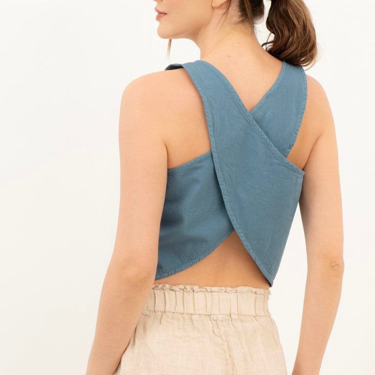 A woman shown from the back wearing a dusty blue wrap-style crop top and light beige linen shorts against a plain white background.