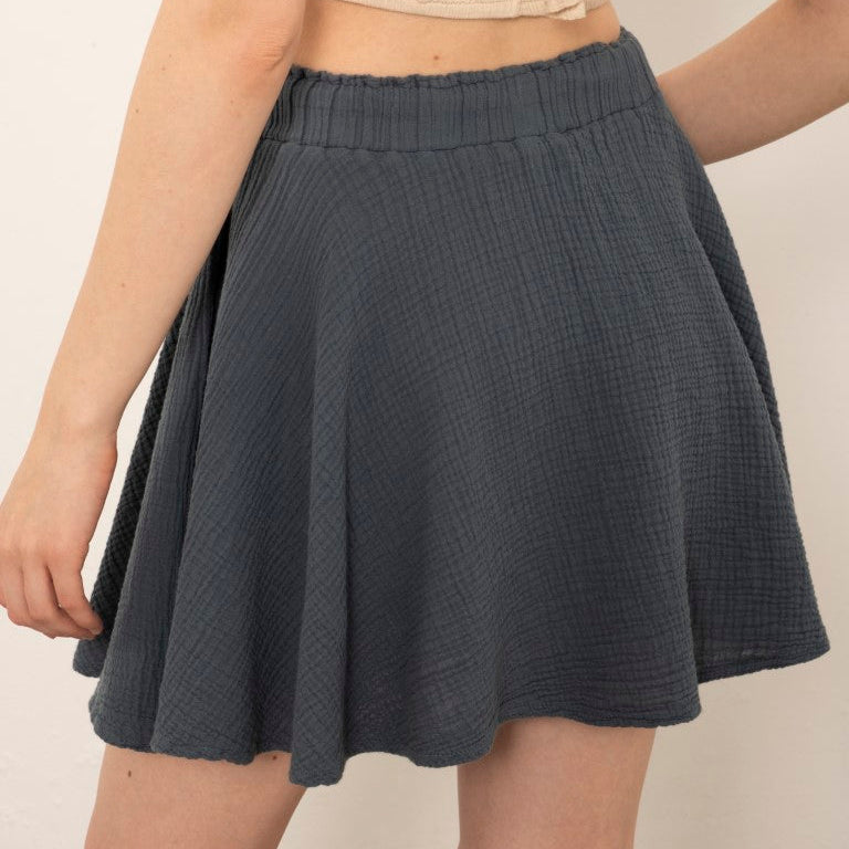 A model wearing a dark gray textured mini skirt and a beige strapless crop top, shown from the back against a plain off-white background.