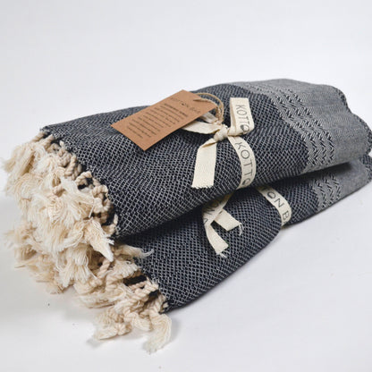 Folded gray towel with tassels and a brown label on a white background