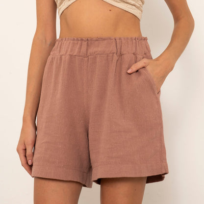 Person wearing a beige top and brown shorts on a plain background