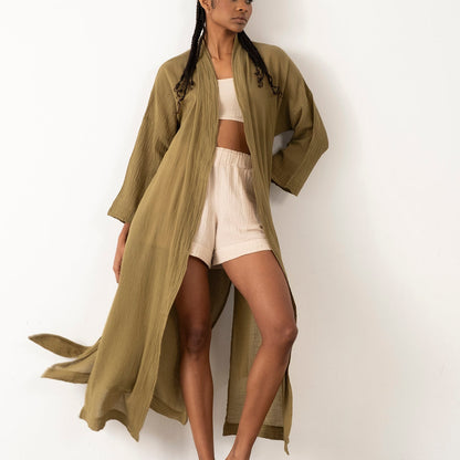 Woman wearing a long olive green coat over a white outfit against a white background