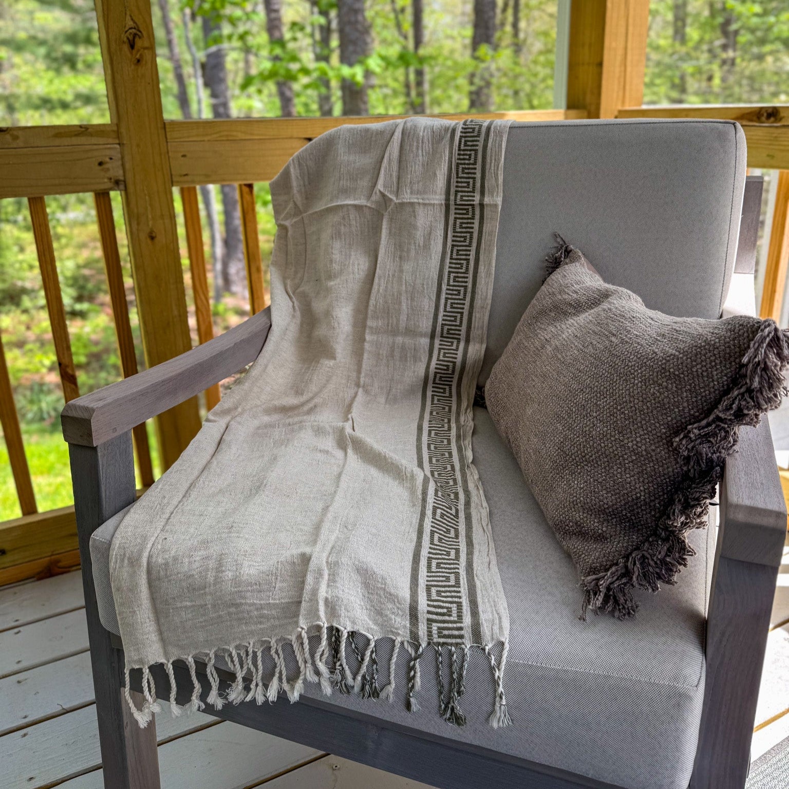 Chair with a Turkish peshtemal towel and pillow on a wooden deck with a forest view
