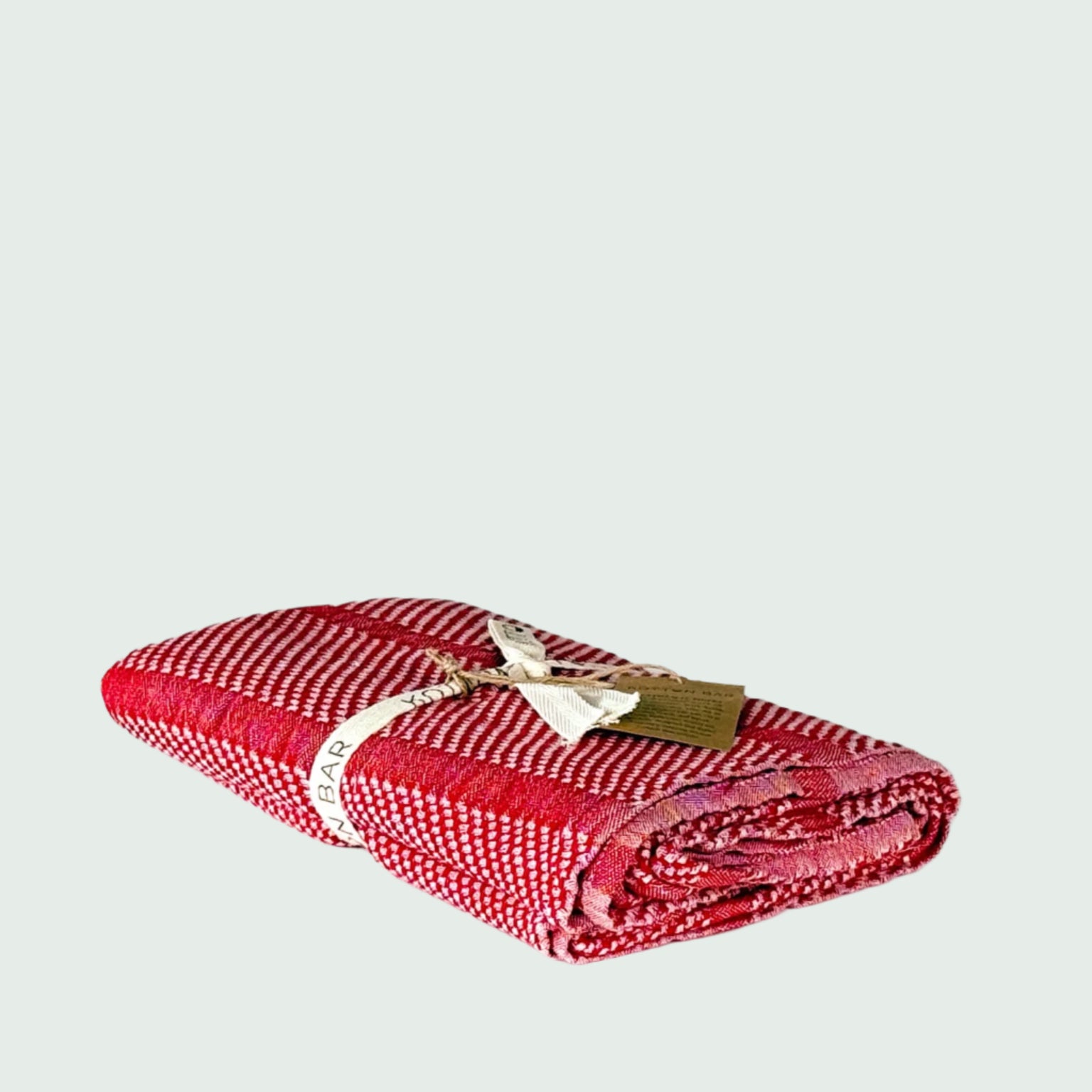 Rolled-up red turkish cotton towel with a tag on a white background