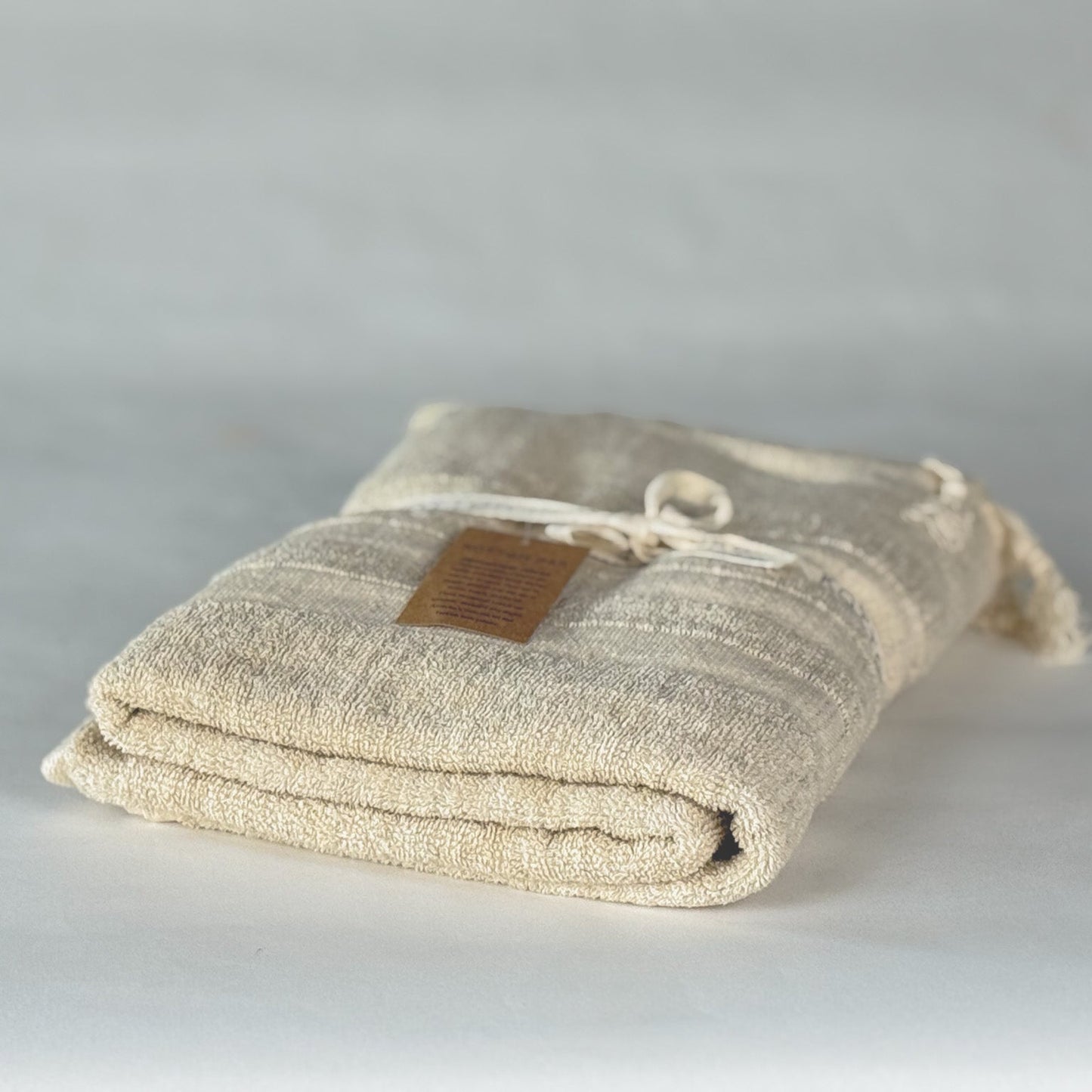 Folded beige fabric turkish cotton towel with a brown label on a light gray background