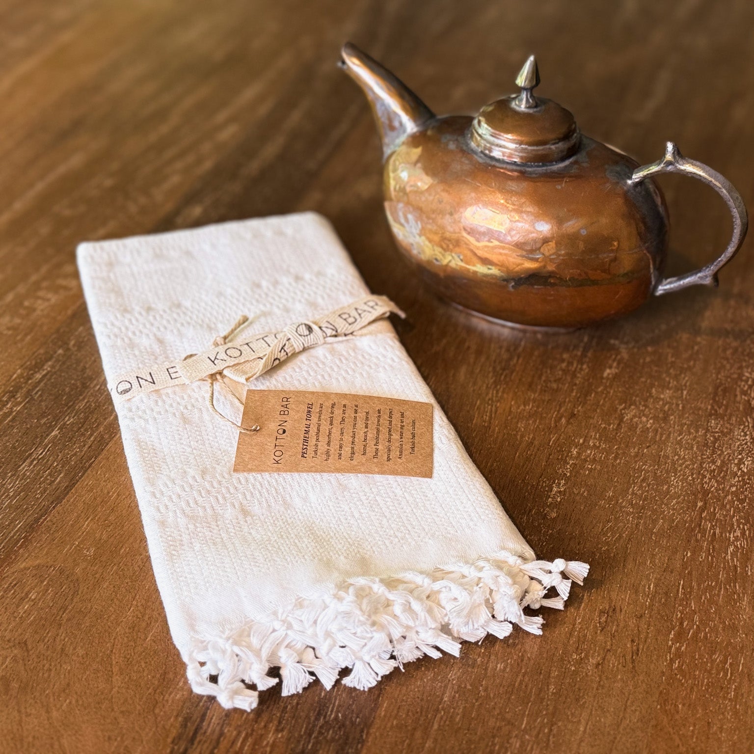 Copper teapot and white towel with lace edge on a wooden surface