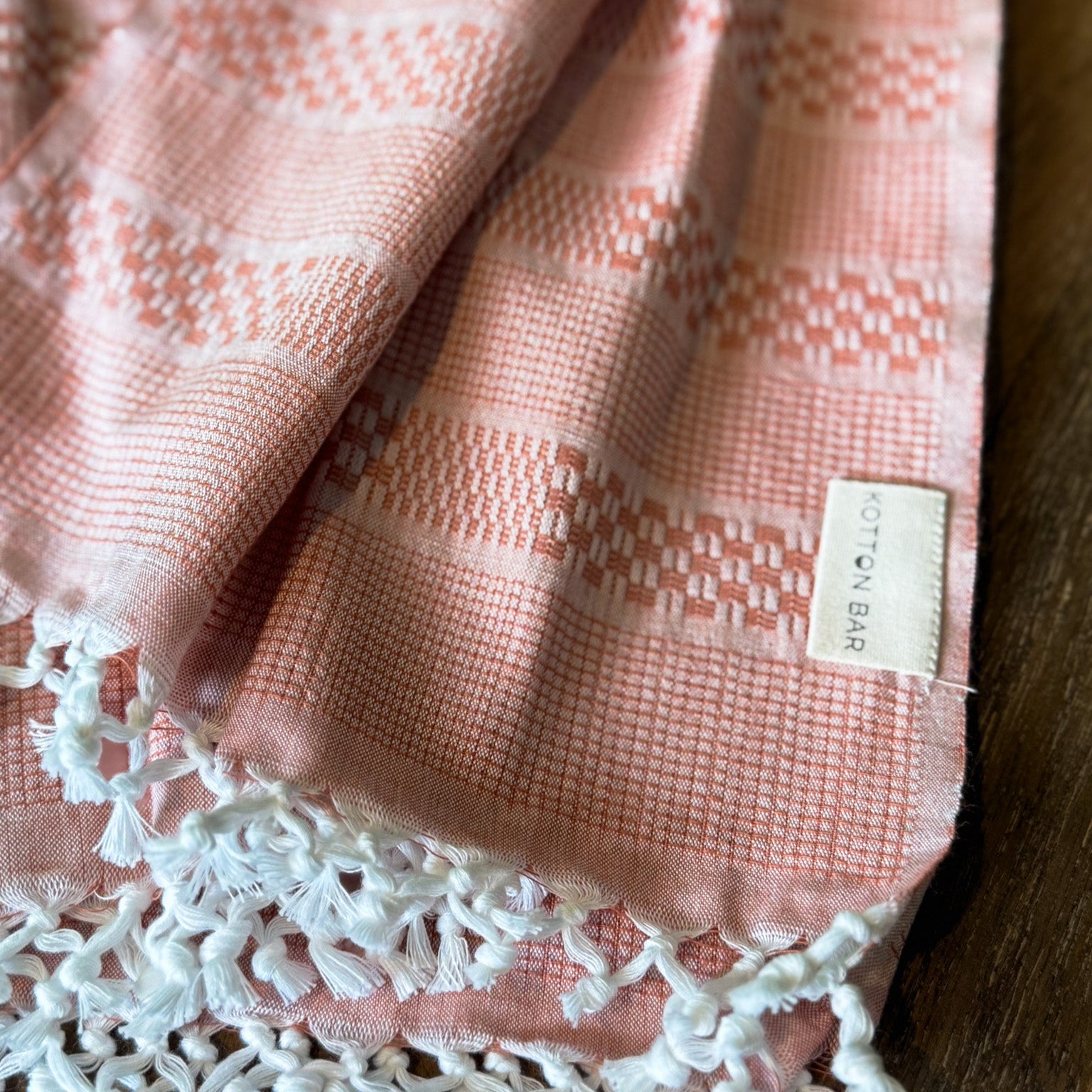 Pink textured fabric with white lace trim and a label on a wooden surface
