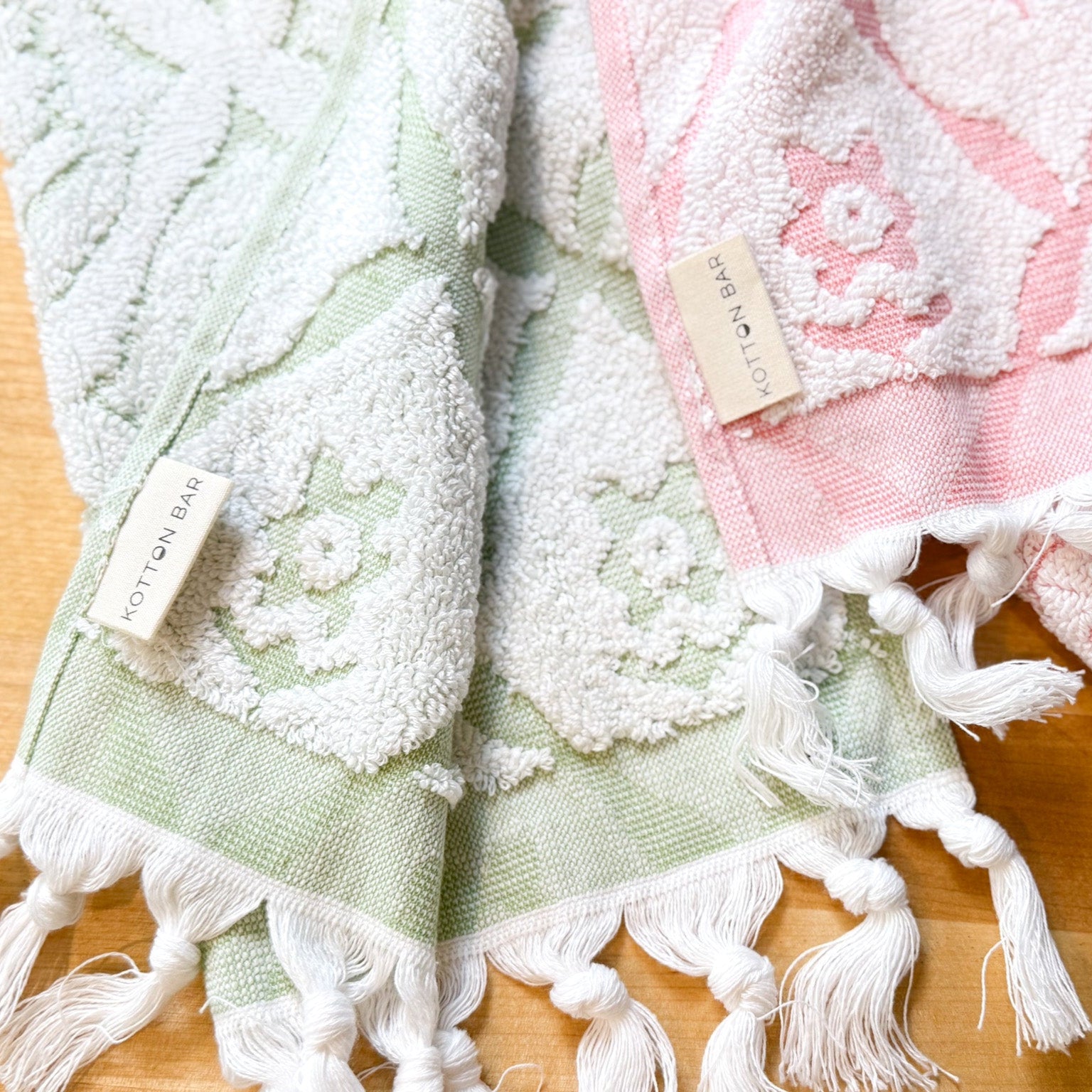 Two textured towels, one green and one pink with tassels, on a wooden surface.