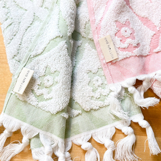 Two textured towels, one green and one pink with tassels, on a wooden surface.