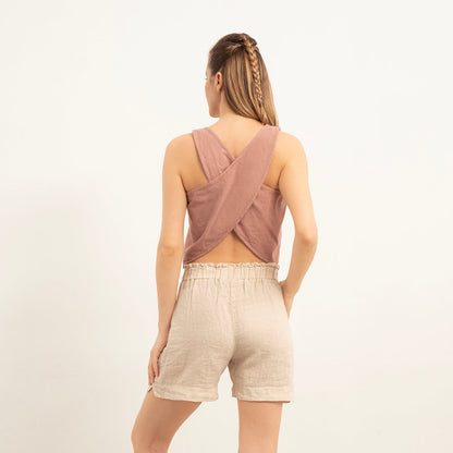 Woman wearing a mauve tank top and beige shorts against a white background
