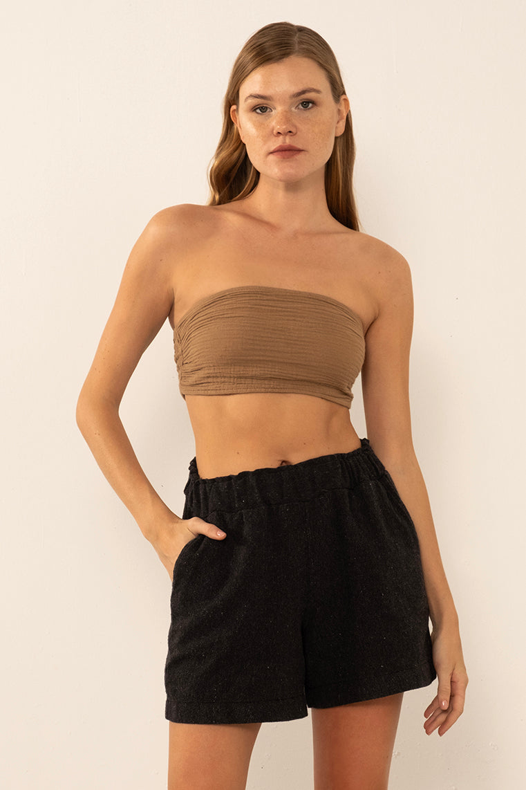 Woman wearing a brown strapless top and black shorts on a plain background